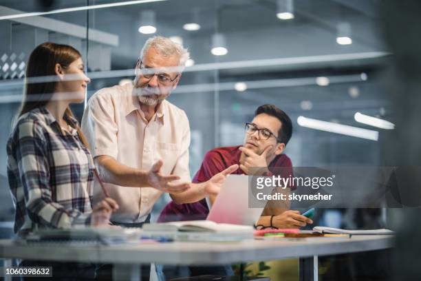 mature professor explaining the lecture to his students while using laptop at campus. - education building stock pictures, royalty-free photos & images