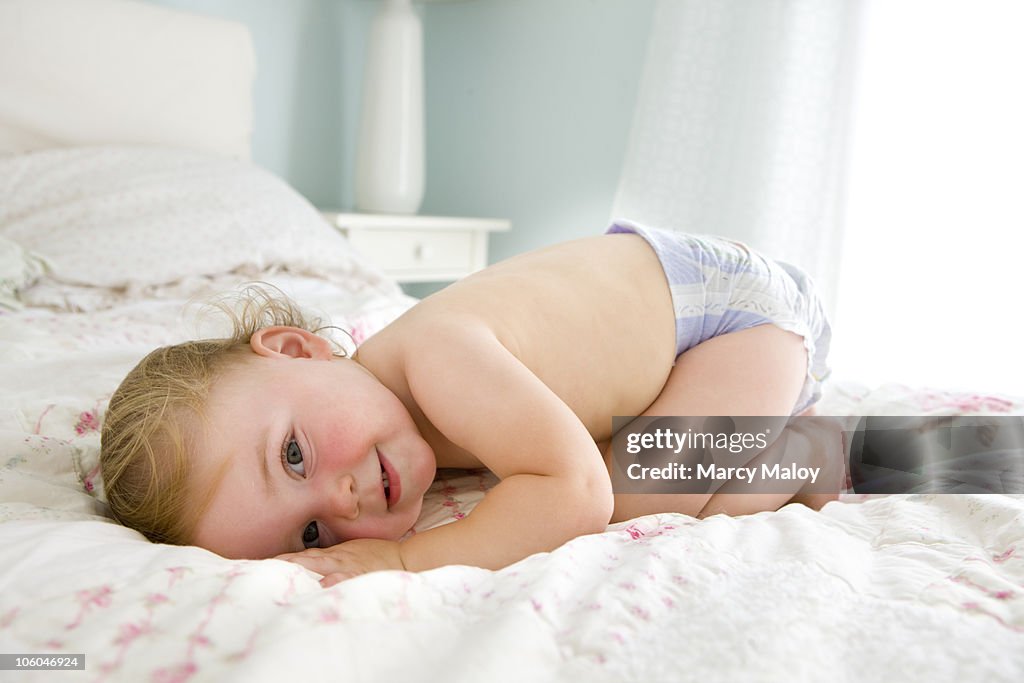 Smiling child on bed wearing a purple diaper