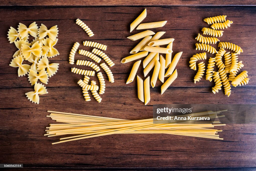 Variety of types and shapes of dry Italian pasta - fusilli, spaghetti, farfalle and penne, top view. Uncooked whole wheat italian pasta. Image with copy space.