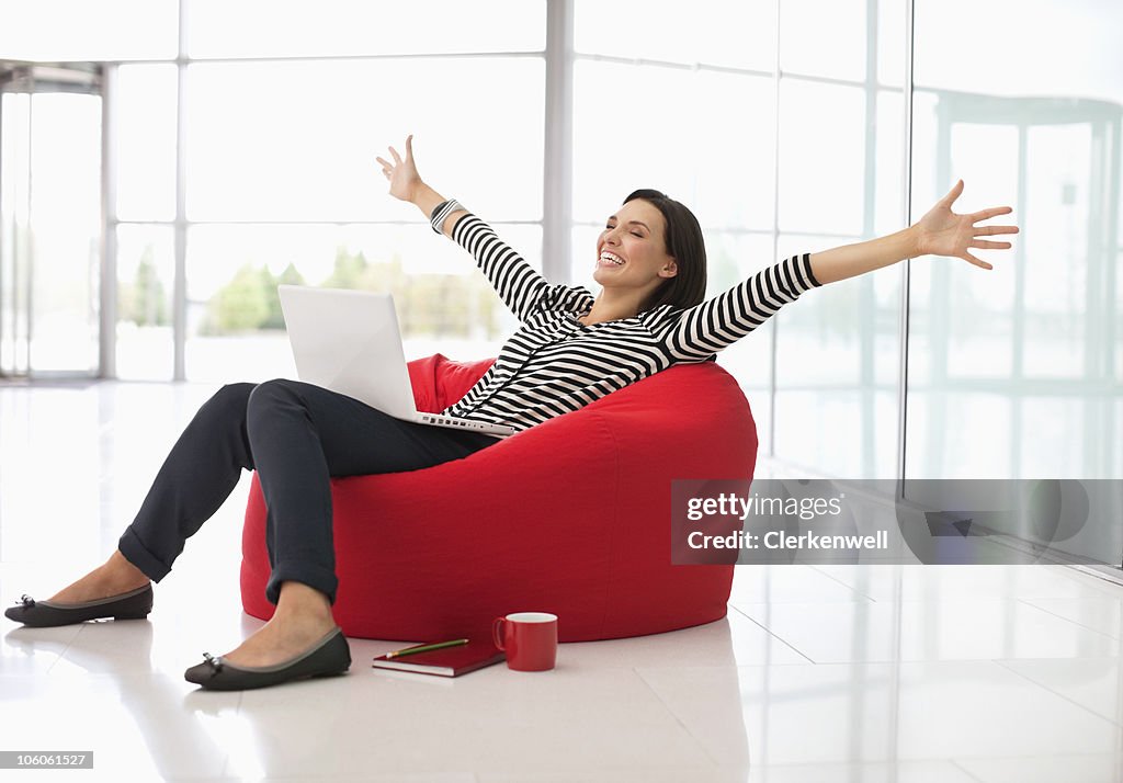 Excited woman sitting on a bean bag with laptop and arms outstretched