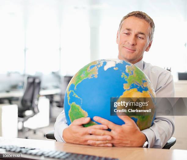 businessman hugging a globe at office desk - world at your fingertips stockfoto's en -beelden