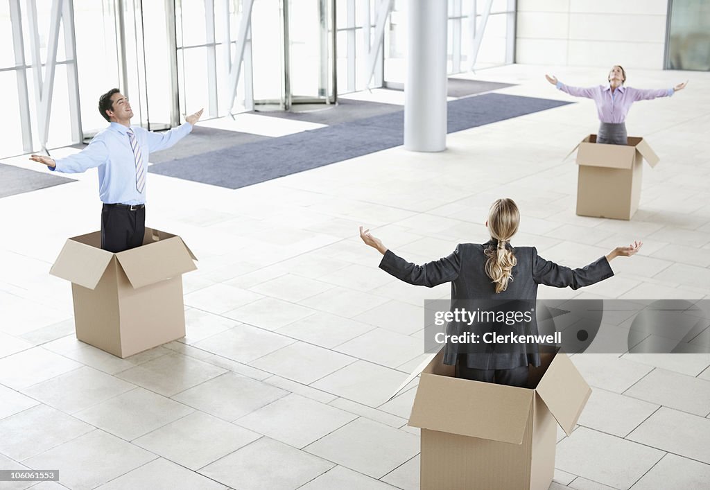 Business colleagues inside cardboard boxes with arms outstretched at new office