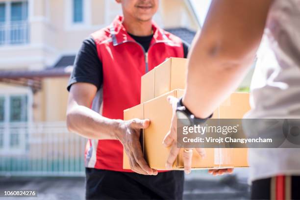 parcel delivery man of a package through a service and customer hand accepting a delivery of boxes from delivery man. - delivery man stock pictures, royalty-free photos & images