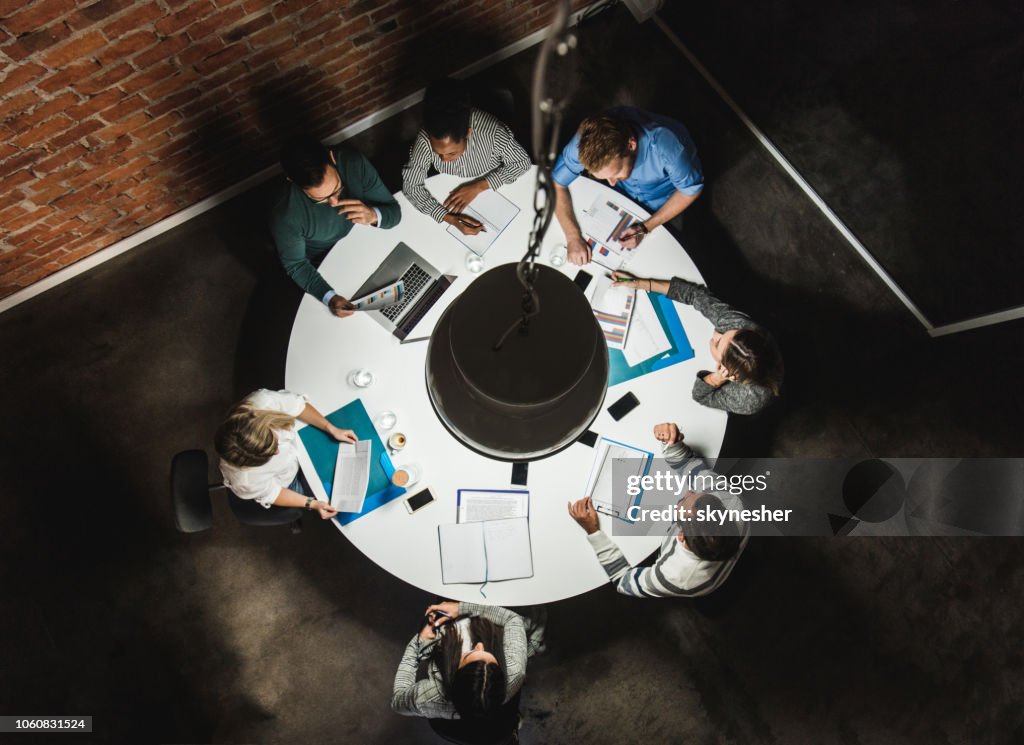 Above view of business colleagues analyzing reports on a meeting at the table.