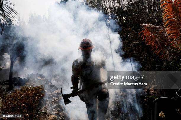 County firefighter Battalion 13 Captain Victor Correa helps put out hotspot in a neighborhood razed by the Woolsey fire on Harvester road November...