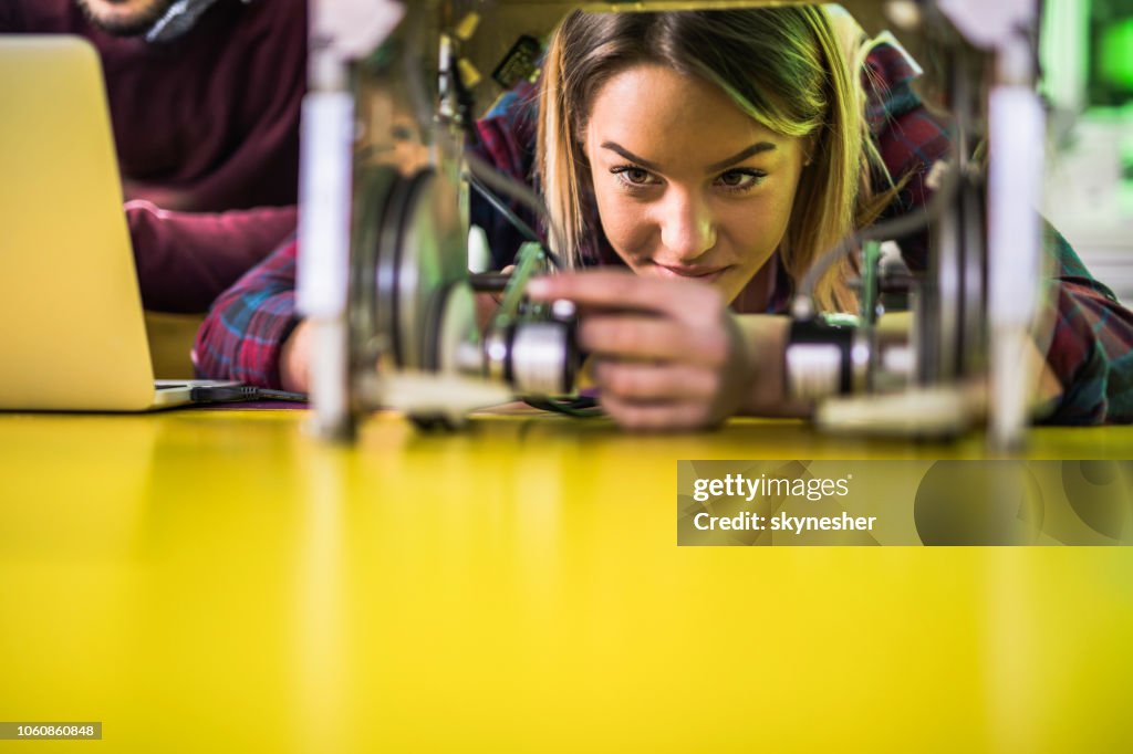 Young smiling woman examining robotic parts in laboratory.