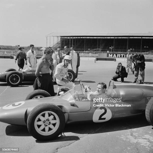 New Zealand race-car designer, driver, engineer and inventor Bruce McLaren on his Cooper T53-Climax car chatting with British Formula One racing...