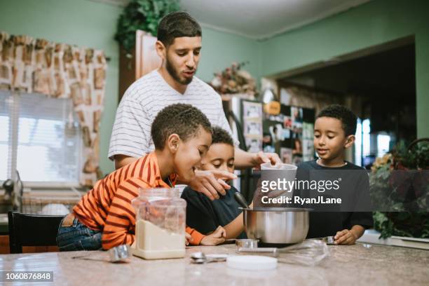 father prepares meal in kitchen with his sons - sibling stock pictures, royalty-free photos & images