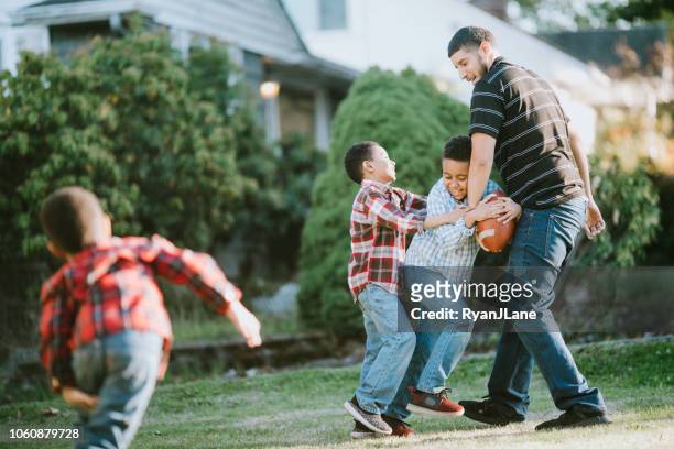 father plays football outside with his sons - american football family stock pictures, royalty-free photos & images