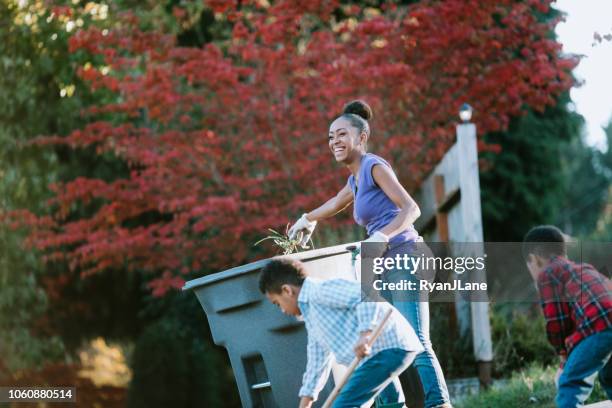 mother works in yard doing chores with her children - wheelie bin stock pictures, royalty-free photos & images