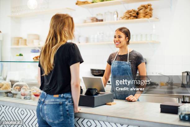 barista smiles at a female customer in a cafe - cafeteria counter stock pictures, royalty-free photos & images