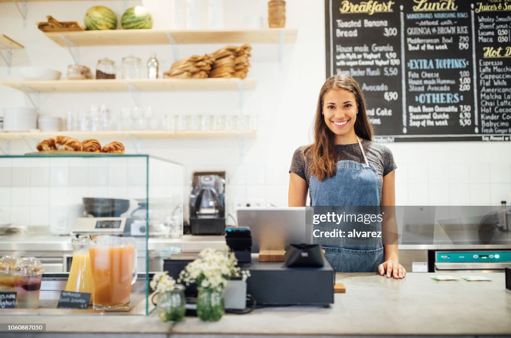 Confident female barista standing behind cafe counter