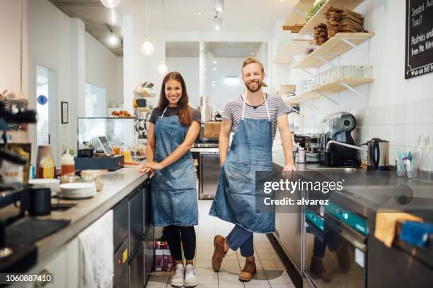 zwei rassen baristas in café-küche - schürze stock-fotos und bilder