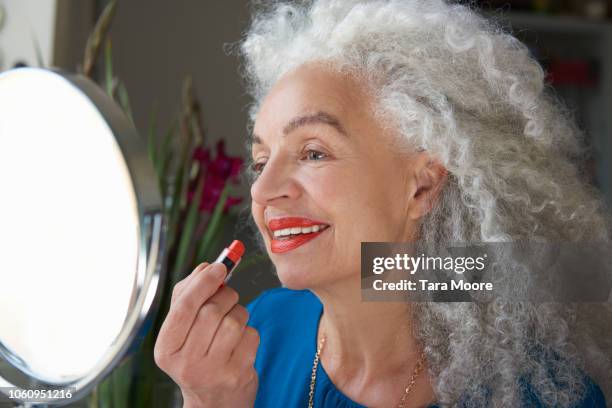 senior woman applying lipstick in mirror - woman gray hair mirror stock pictures, royalty-free photos & images