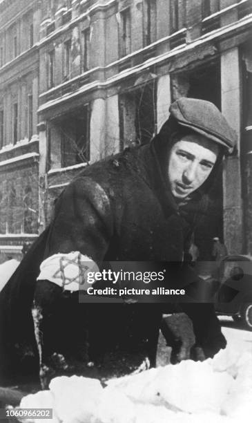 Jewish inhabitant of the Warsaw Ghetto with the star of David removes snow from the streets .