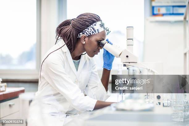 mujer científico trabajando en el laboratorio, utilizando un microscopio - biopsy fotografías e imágenes de stock