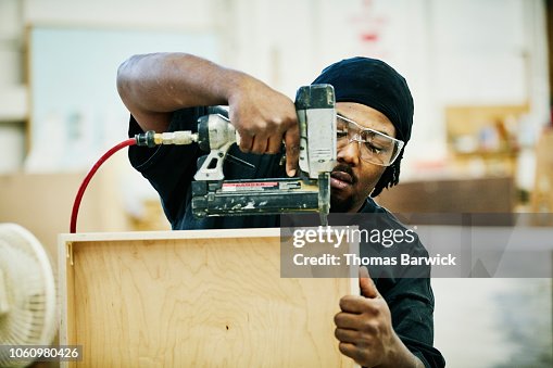 Woodworker nailing together drawer in cabinet shop