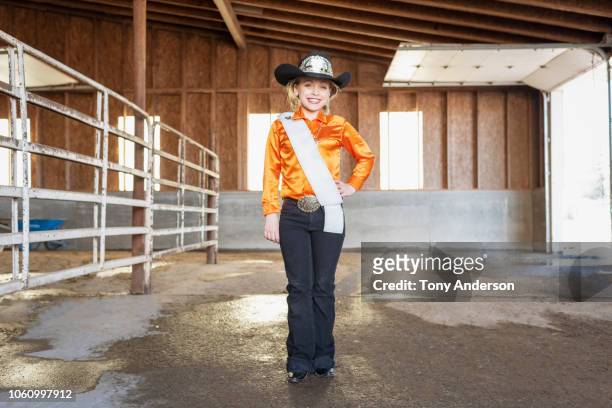young cowgirl pageant contestant standing in barn - sash stock pictures, royalty-free photos & images