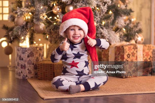 christmas and new year concept. child boy in red hat smiling under a christmas tree. - under value stock pictures, royalty-free photos & images