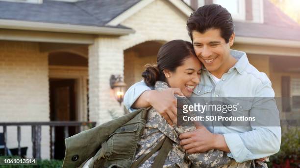 mid-adult woman in uniform is pulled into hug by a mid-adult man. - mid adult men stock pictures, royalty-free photos & images