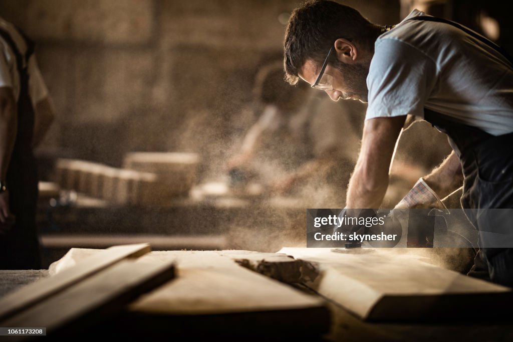 Junge Tischler mit Sander während der Arbeit an einem Stück Holz.