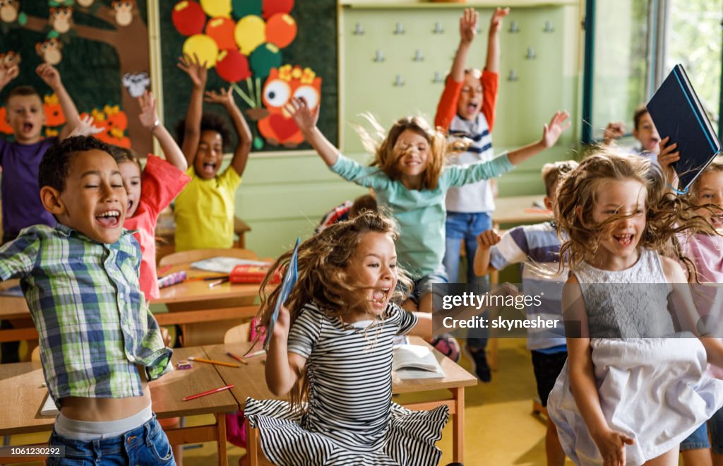 Large group of joyful elementary students jumping in the classroom.