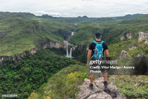 young adult hiker on rocky edge looking at beautiful cerrado landscape with waterfalls and river in the green forest, mirante da janela peak, chapada dos veadeiros, goias state, central brazil - central and south america stock pictures, royalty-free photos & images