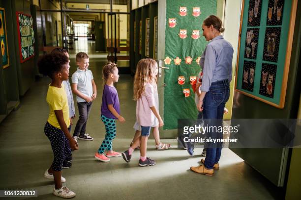 happy female teacher welcoming elementary students in the classroom. - entering school stock pictures, royalty-free photos & images
