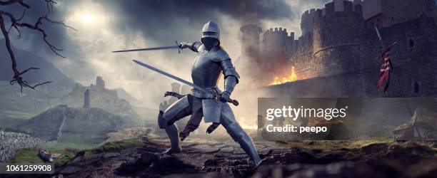 medieval knight in armour holding two swords near burning castle - medieval sword stock pictures, royalty-free photos & images