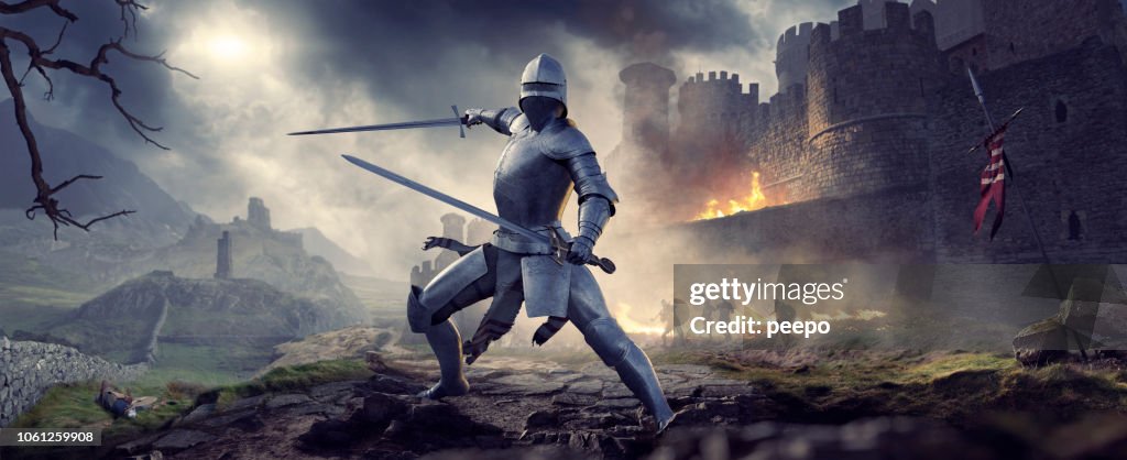 Medeltida riddare i rustning som håller två svärd nära brinnande slott
