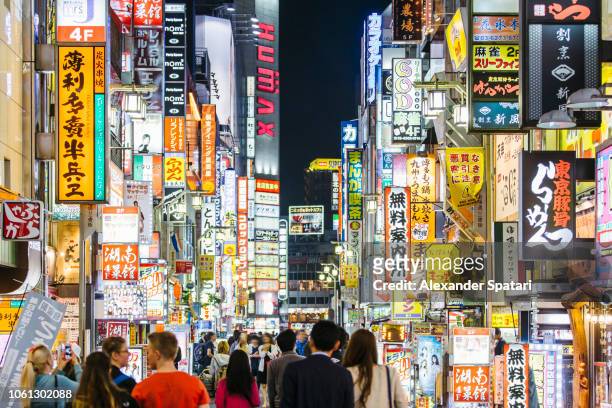 crowds of people walking among illuminated neon signs at kabukicho road in shinjuku district, tokyo, japan - downtown neon stock-fotos und bilder