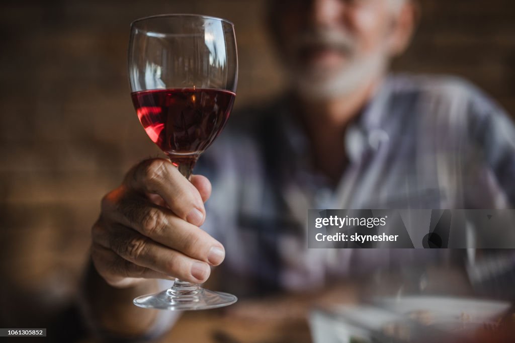 Close up of unrecognizable senior man holding glass of red wine.
