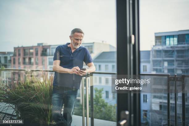 midaged bärtigen blick auf mobile auf balkon in berlin - nordeuropäischer abstammung stock-fotos und bilder