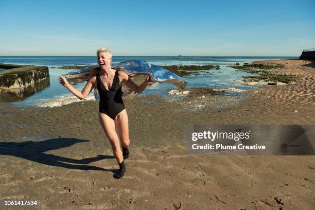 woman with foil blanket running on beach - standing water stock pictures, royalty-free photos & images