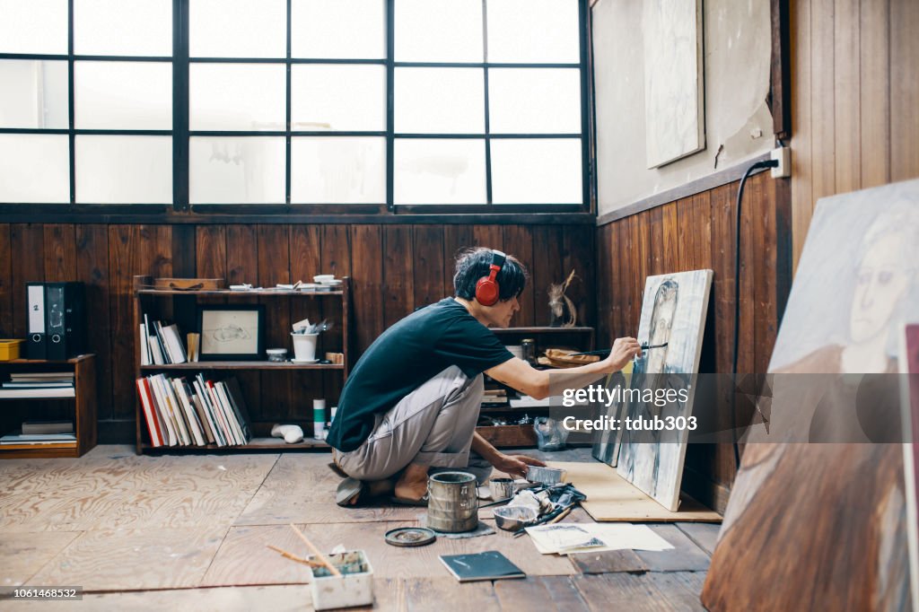 Reifer Mann malen mit Ölfarbe in seinem Atelier beim Tragen von Kopfhörern
