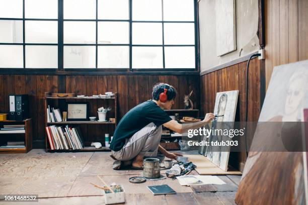 mature man painting with oil paint in his studio while wearing headphones - male artist painting stock pictures, royalty-free photos & images