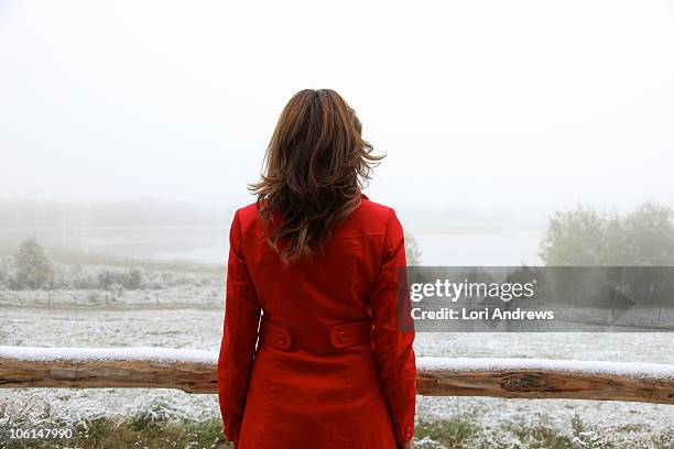 woman in red coat overlooking snowy landscape - red coat stock-fotos und bilder