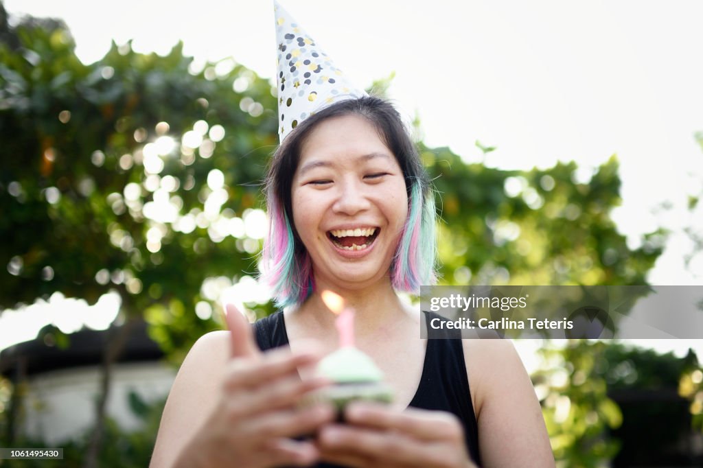 Woman holding a birthday cupcake wearing a party hat