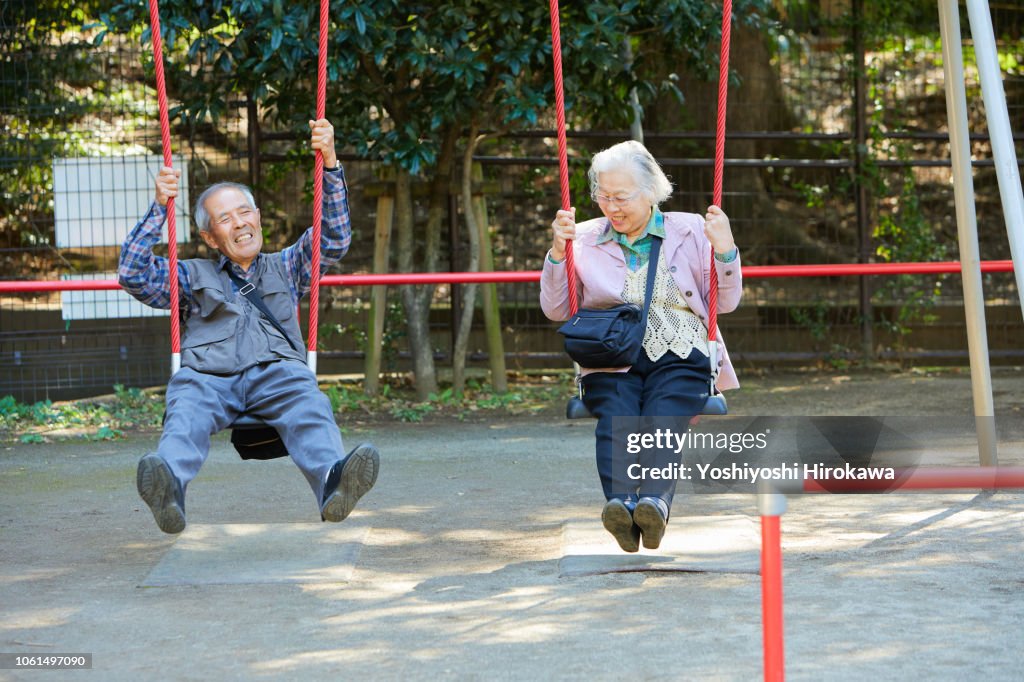 Smiling seniors who sitting on a swing while walk in the park