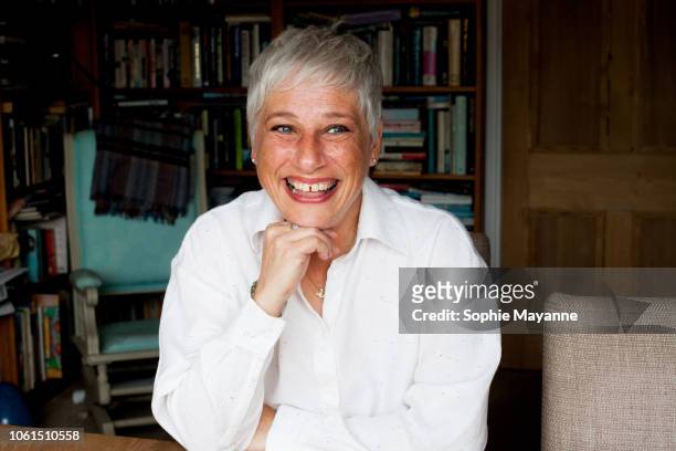 A mature woman smiling  in front of a bookshelf