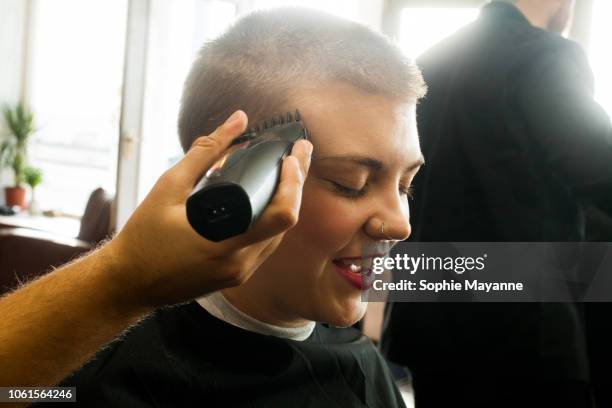 a young woman cutting her hair at a barbers - head shave stockfoto's en -beelden