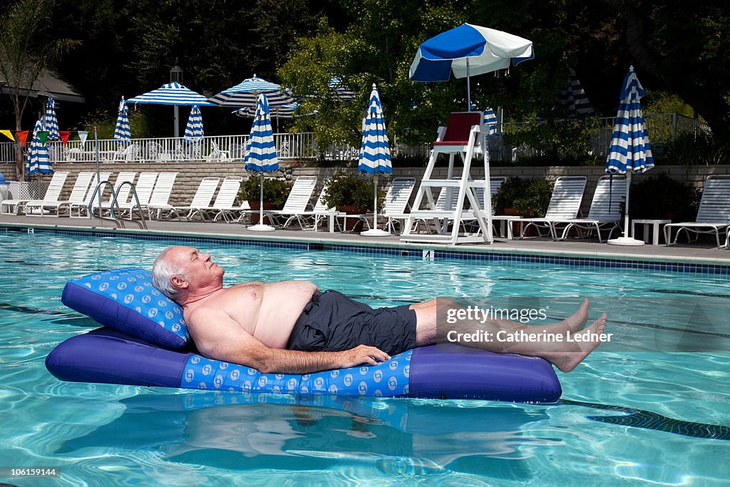 Senior man floating on raft in pool