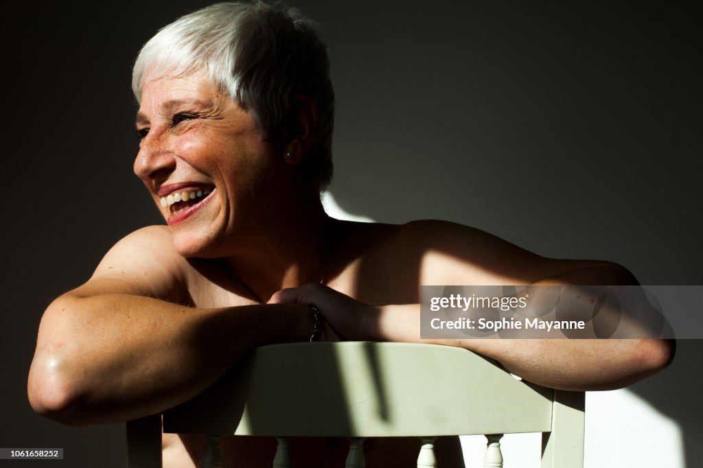 A mature woman leaning on the back of a chair in the sunlight