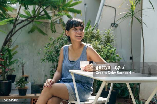 happy confident asian woman drinking smoothie in the garden at home. short highlighted hair - showus skin stock pictures, royalty-free photos & images