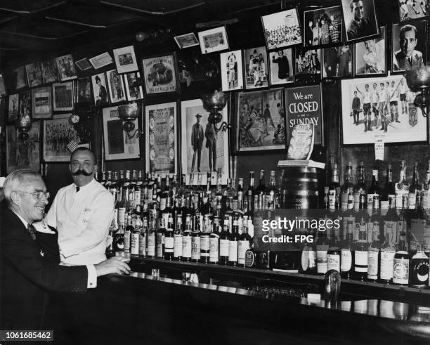 Well-stocked bar at Bill's Gay Nineties, a speakeasy located at 57 East 54th Street, New York City, circa 1940. The barman is wearing a large fake...