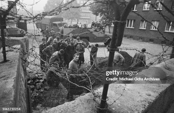 East German guards examine a large hole or tunnel in the ground on Harzer Strasse, on the Berlin Wall, Germany, October 1962.