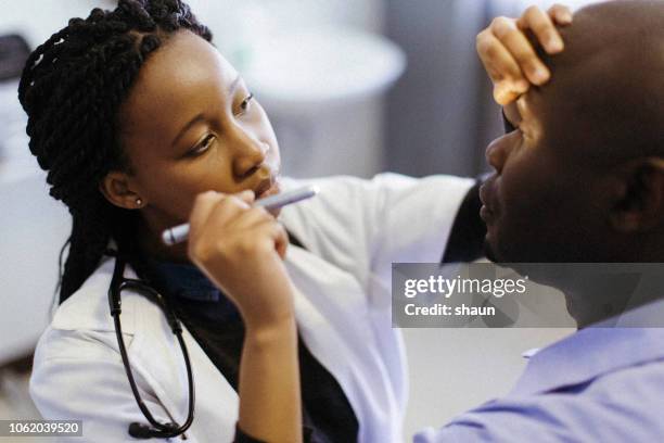 a doctor performing an eye examination - african ethnicity doctor stock pictures, royalty-free photos & images