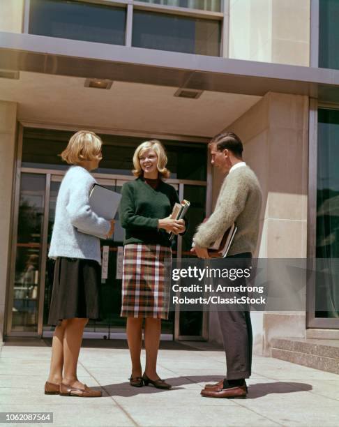 1960s THREE COLLEGE STUDENTS TALKING HOLDING TEXTBOOKS