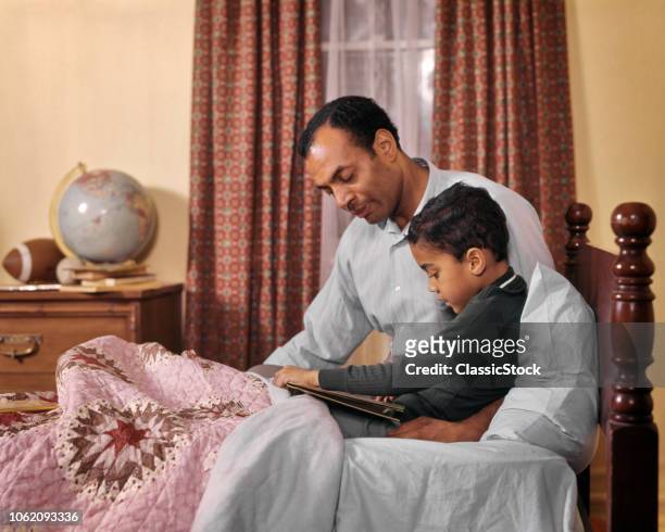1960s 1970s AFRICAN AMERICAN MAN FATHER AND BOY SON READING BEDTIME STORYBOOK BED ROOM TOGETHER TEACHING LEARNING LOVE