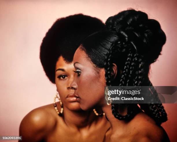 1960s 1970s TWO AFRICAN AMERICAN WOMEN FACES BARE SHOULDERS ONE WITH AFRO HAIR STYLE LOOKING AT CAMERA PAST OTHER WITH BRAIDS